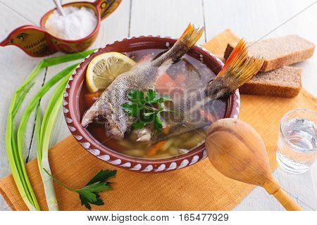 Traditional Russian fish soup in a clay bowl on a wooden table. Rustic style