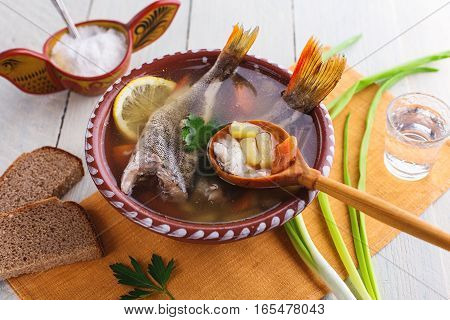 Traditional Russian fish soup in a clay bowl on a wooden table. Rustic style