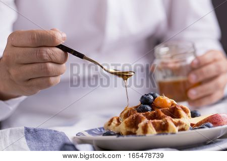 Blueberry apple waffle with honey set on a dish with a chef's hand holding spoon for a jar of honey ready to serve.