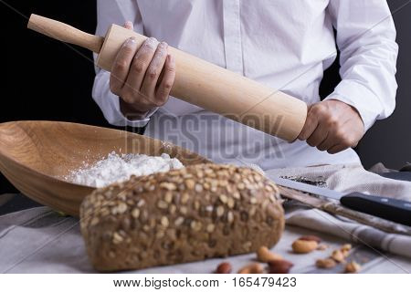 Whole grain bread put on kitchen napkin decorated with almond with a chef holding dough roller at the background.