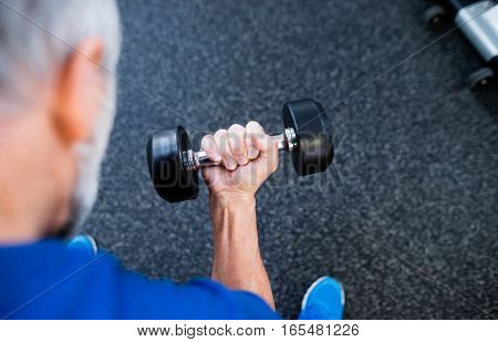 Unrecognizable senior man in sports clothing in gym working out with weights.