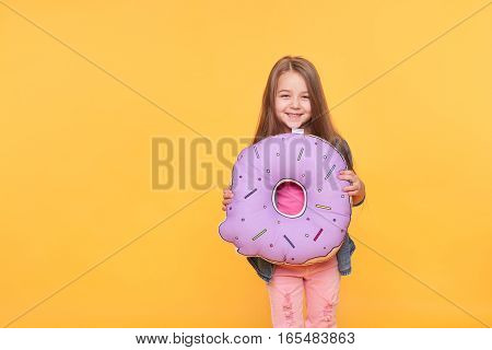 Little girl holding big donut over yellow background. Cute preschool kid smiling with giant null numeral isolated on vibrant color wall. Zero calories, Food and sweets concept