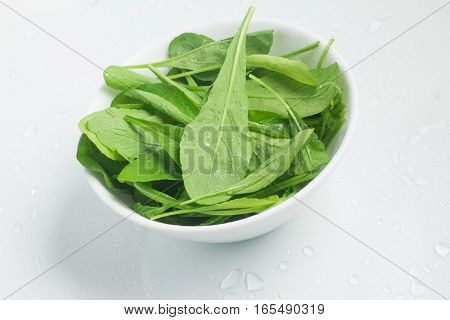 Arugula Leaves into a bowl over a white background
