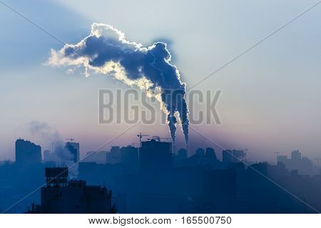 Power plant with smoking chimneys. City in the background.
