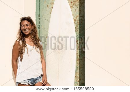 young girl stand with a surfboard in front of grunge door.