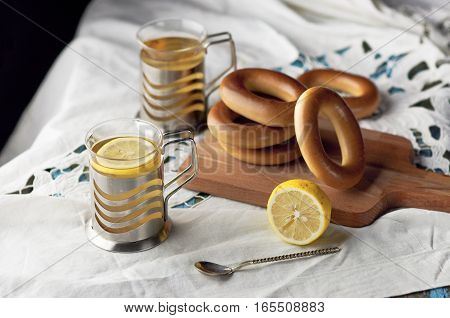Mug of tea with lemon and bagels on a wooden background. Tea with lemon Baking bagels white tablecloth.