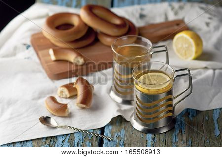Mug of tea with lemon and bagels on a wooden background. Tea with lemon Baking bagels white tablecloth.