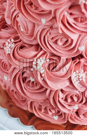 Gorgeous two-tier cake covered in roses made of butter cream icing sitting on a cake pedestal with background