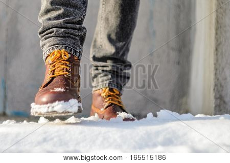 Man walks in the snow street. Feet shod in brown winter boots. Winter walks concept