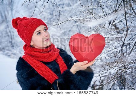 Love and valentines day concept. Portrait of woman holding red polygonal paper heart shape and looking to the side at copy space, over winter landscape