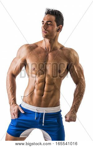 Attractive young man with muscular naked body listening to music with earphones, isolated on white background