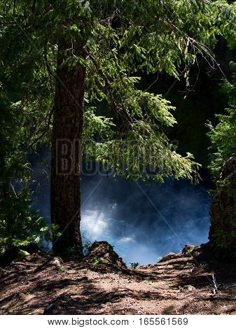 The wild waters and spray from the bottom of Koosah Falls on the McKenzie River in the Willamette National Forest in Western Oregon framed by fir trees and a cliff on a summer day.