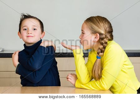 A pretty little girl blows a hand kiss to her cute brother at home in the kitchen
