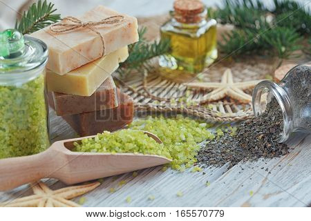 Natural sea salt and handmade soap with branch of pine and seaweed on white wooden background. SPA concept.