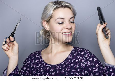 Young female hairdresser with scissors and comb advertising for a cosmetology school or a salon. The image depicts trendy styles and hair color.