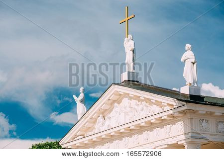 Vilnius Lithuania. Close Pediment Of Cathedral Basilica Of St. Stanislaus, St. Vladislav With Three Statues: St. Elena With Cross, St. Stanislaus, St. Casimir, Relief Sculpture Decoration, Blue Sky