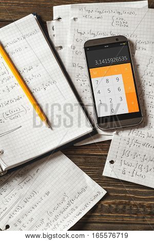 Solving mathematical problems in a notebook .  Phone with calculator app on wooden desk.