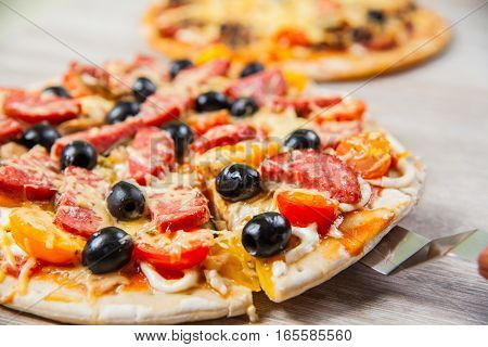 Cook takes a shovel one piece of pizza with cheese olives and salami mushrooms and tomatoes. On a wooden stand.