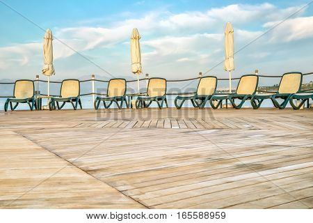 Deserted solarium with wooden decking sun loungers and folded sun parasol after a rain on a background of sea and blue sky with white clouds in a summer day. The foreground is blurred