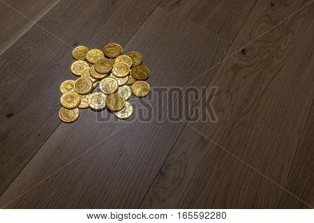 A pile of gold coins shimmer in the light situated on wide oak planks.
