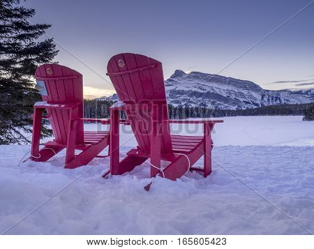 BANFF, ALBERTA - JAN 15: Red Chairs at Two_jack Lake with Parks Canada logos on January 15, 2017 iin Banff National Park, Alberta, Canada. Rundle Mountain is in the background.