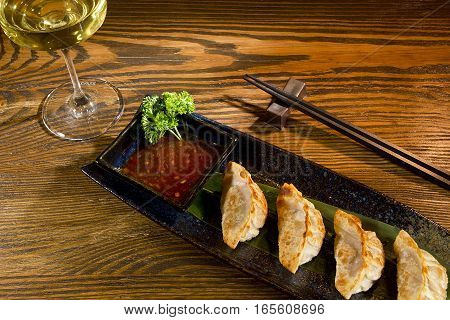 Yaki gedza with sauce in a ceramic pot on a wooden table