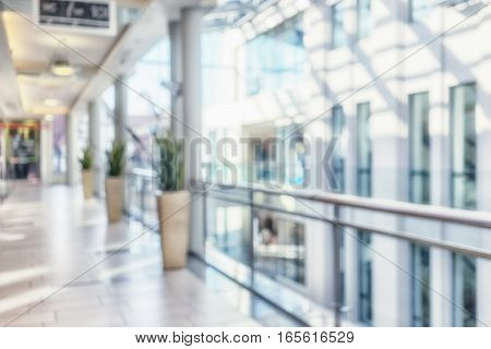 Bright corridor with perspective lines and columns with fresh flowers in pots on the background of the windows in the interior of a modern building. Blurry