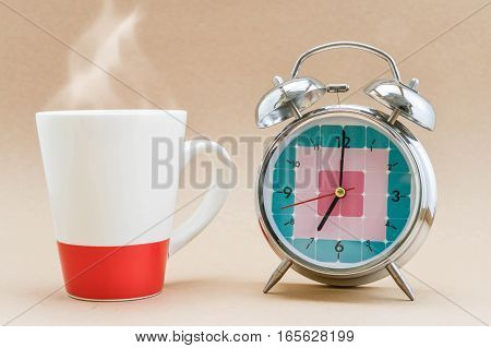 Alarm clock is showing time for 7 AM and a cup of coffee with smoke at site for mornong coffee