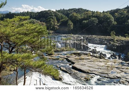 Widespread cascade with flat rocks surrounded by green trees in Kagoshima