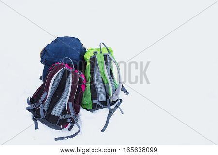Three hiking backpacks in snow. Adult and kids backpacks isolated on white background. Copy space. Family hiking on beautiful cold winter day. Snowlakes on backpacks.