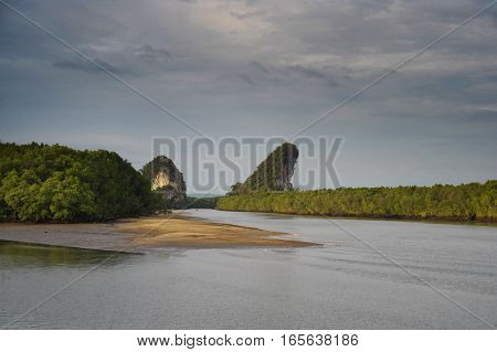 amazing beautiful scenic landscape view of Krabi river in Thailand South Asia with rocks covered with vegetation next to a little sand beach under a stormy blue sky in tourism and travel destination concept