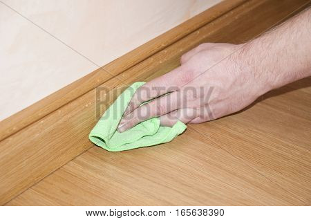 Close up of hand cleaning the wooden oak parquet floor and skirting board