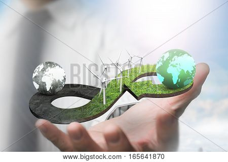 Green circular economy concept. Hand showing arrow infinity symbol of grass texture with wind turbines and two globes of different colors.
