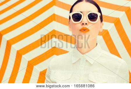 Fashion portrait of a beautiful woman wearing white chemise and sunglasses with bright painted lips next to a striped background