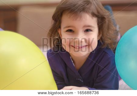 Smiling cute little girl lying on bed with balloons