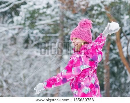 Happy girl smiling outdoors play in snow on cold winter day. Child enjoying in snowy park. Outdoor fun for childhood Christmas vacation.