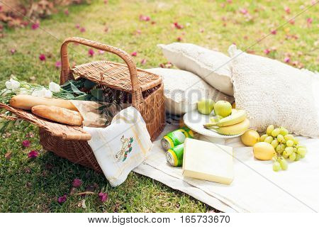 Picnic on the grass. Straw basket, flowers, fruit and bread