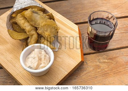 Fish and chips with a tartar sauce and a glass of red wine, on a wooden table with copy space. An English dish served in a traditional Spanish cucurucho, cone, and with a chato glass