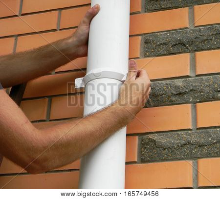 Man installing rain gutter system downspout pipe