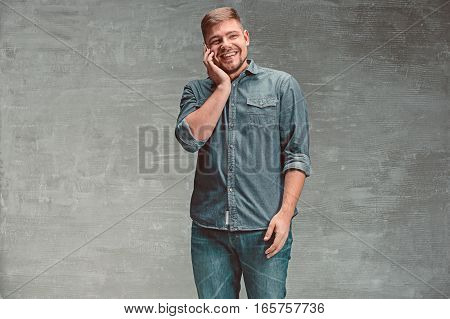 The young smiling caucasian businessman on gray studio background talking on cell phone