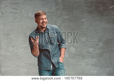 The young smiling caucasian businessman on gray studio background with mobile phone