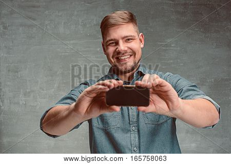 The young smiling caucasian businessman on gray studio background with mobile phone