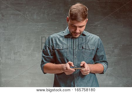 The young smiling caucasian businessman on gray studio background with mobile phone