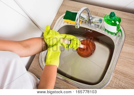 Close-up Of Person Using Plunger In The Kitchen Sink