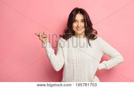 Happy smiling beautiful young woman in white winter sweater showing copyspace over vivid pink color background