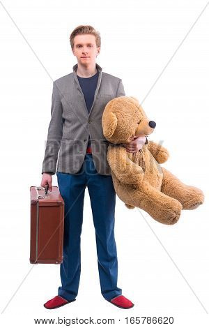 Portrait of young man with old fashioned suitcase and large stuffed toy bear on white background.