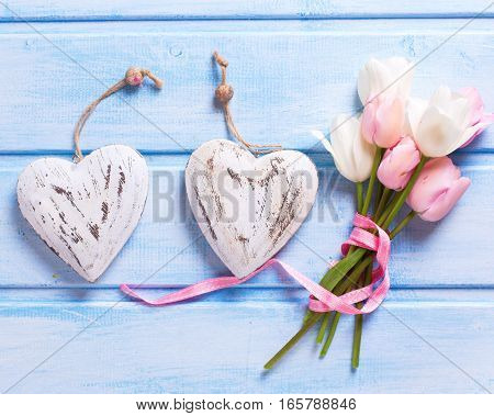 White and pink spring tulips and two decorative hearts on blue background. Pastel colors. Shubby chic. Selective focus.