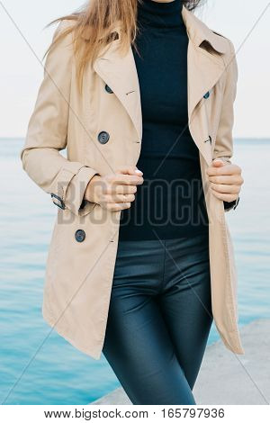 Slender Girl In A Beige Coat And Black Pants On The Beach