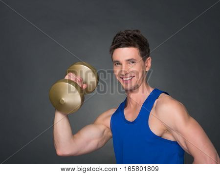 Handsome power athletic man in training pumping up muscles with dumbbell in a gym. blue t-shirt