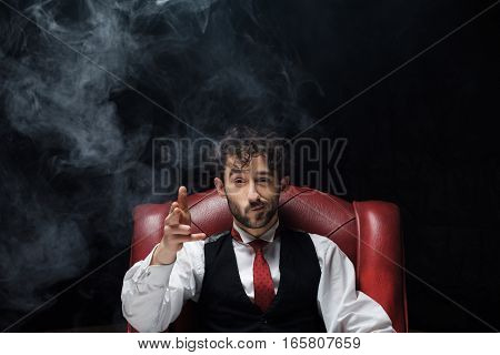 Businessman with smoking gun finger red. red chair on a black background
